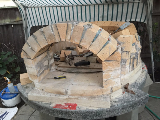 The image shows a brick arch and half dome, showing the beginning skeleton of the pizza oven before the top bricks are added and any finishing has been completed.